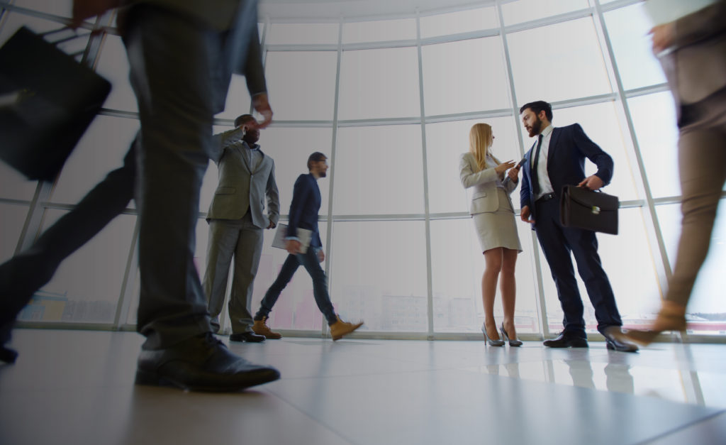 Business men and women walk through an office while discussing business matters.