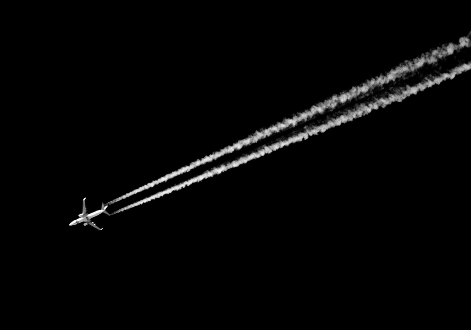 An aircraft shooting across a dark sky and leaving behind white trails.