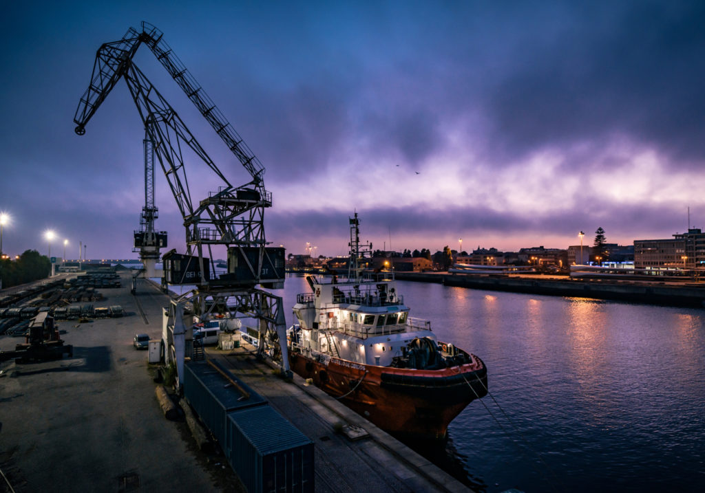 A ship being loaded with freight by the side of a dock.