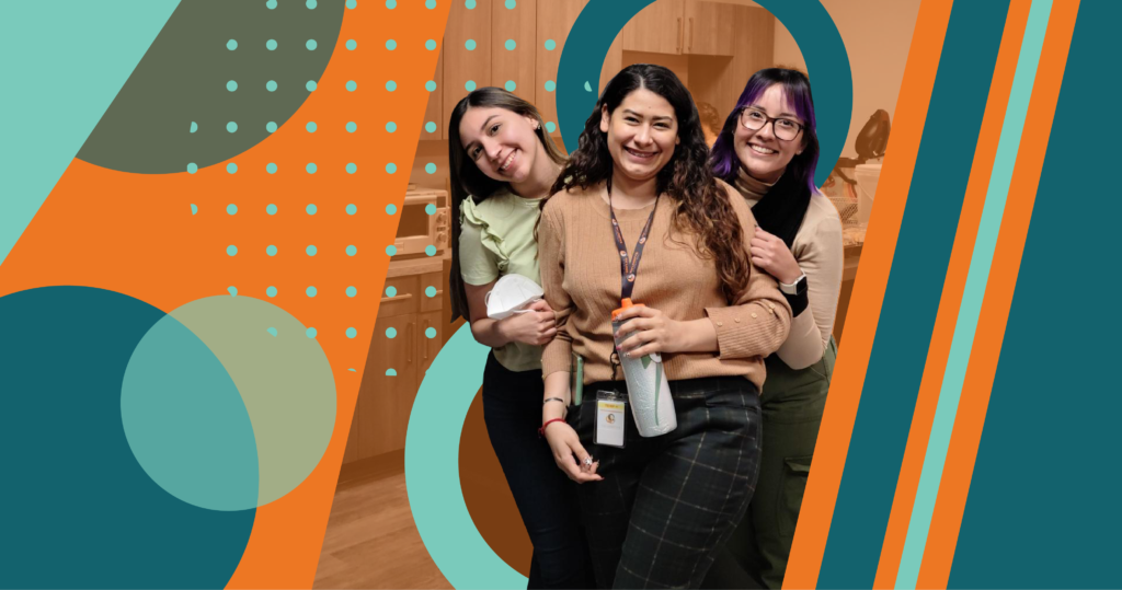 Three girls posing for a picture with a bottle of wine.